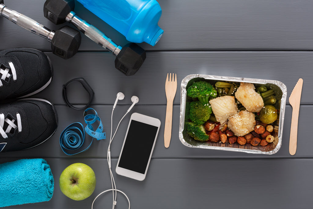 image of weights, tennis shoes, fitness tracker, water bottle, apple and vegatables on a table