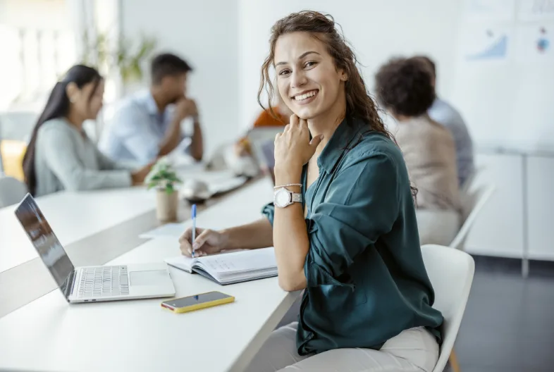 women smiling at camera while taken notes in open setting