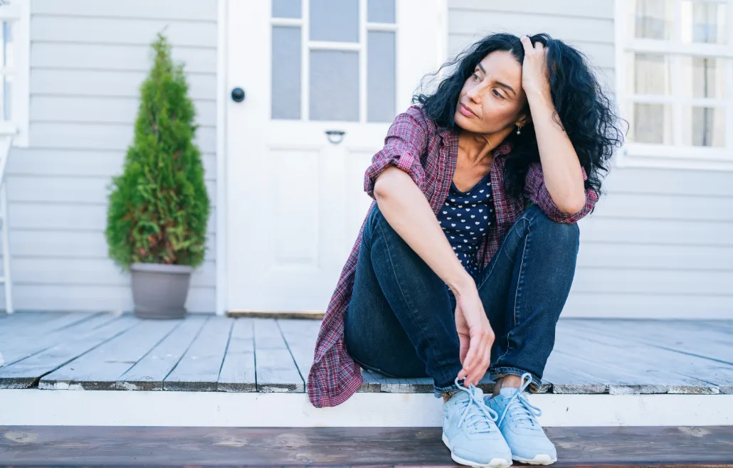 Woman sitting on her porch supporting head with arm resting on knee as she looks away