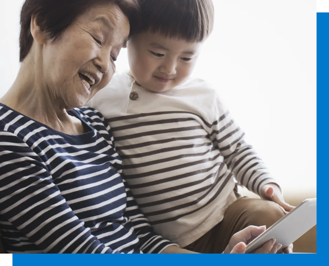 elderly woman holding child looking at tablet smiling